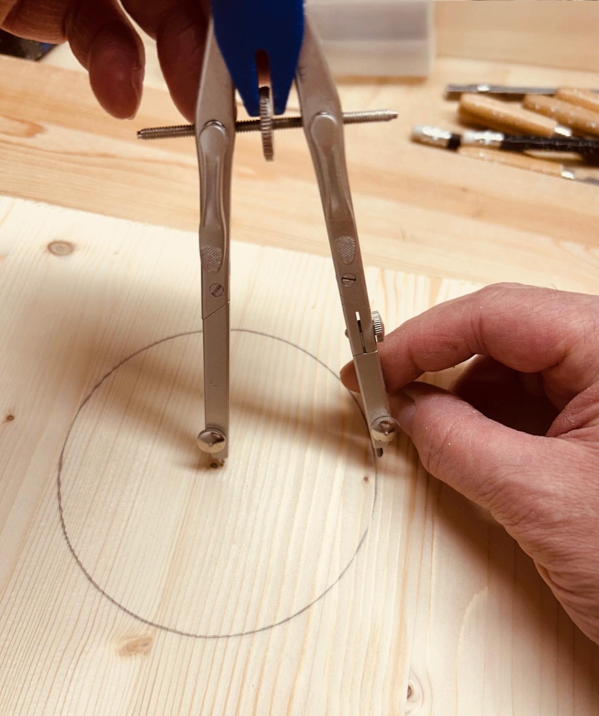 Hände zeichnen mit einem Zirkel einen Kreis auf ein Holzbrett