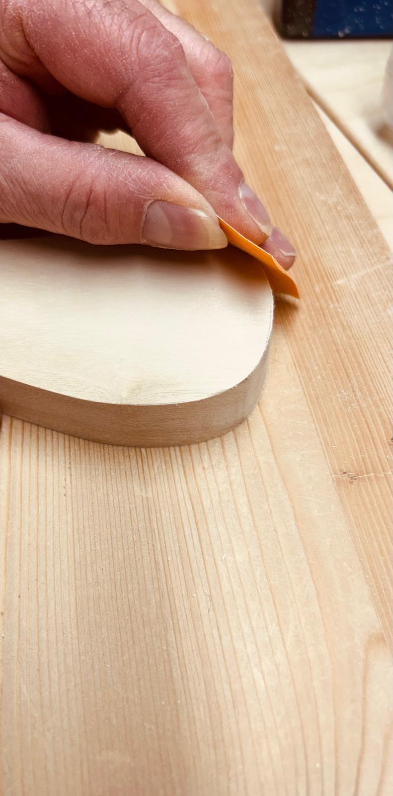 Hand schleift die Kante eines Holzteils mit Schleifpapier
